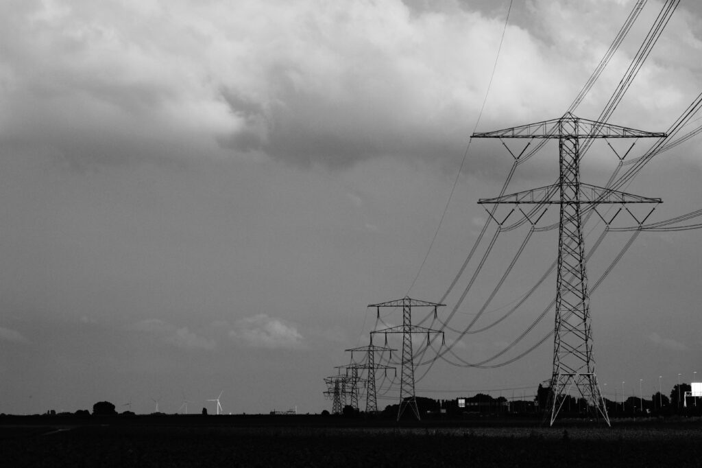 Black and white image of power lines stretching across a rural landscape under cloudy skies.